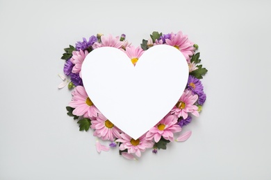 Beautiful chamomile flowers and heart shaped paper card on white background, top view with space for text