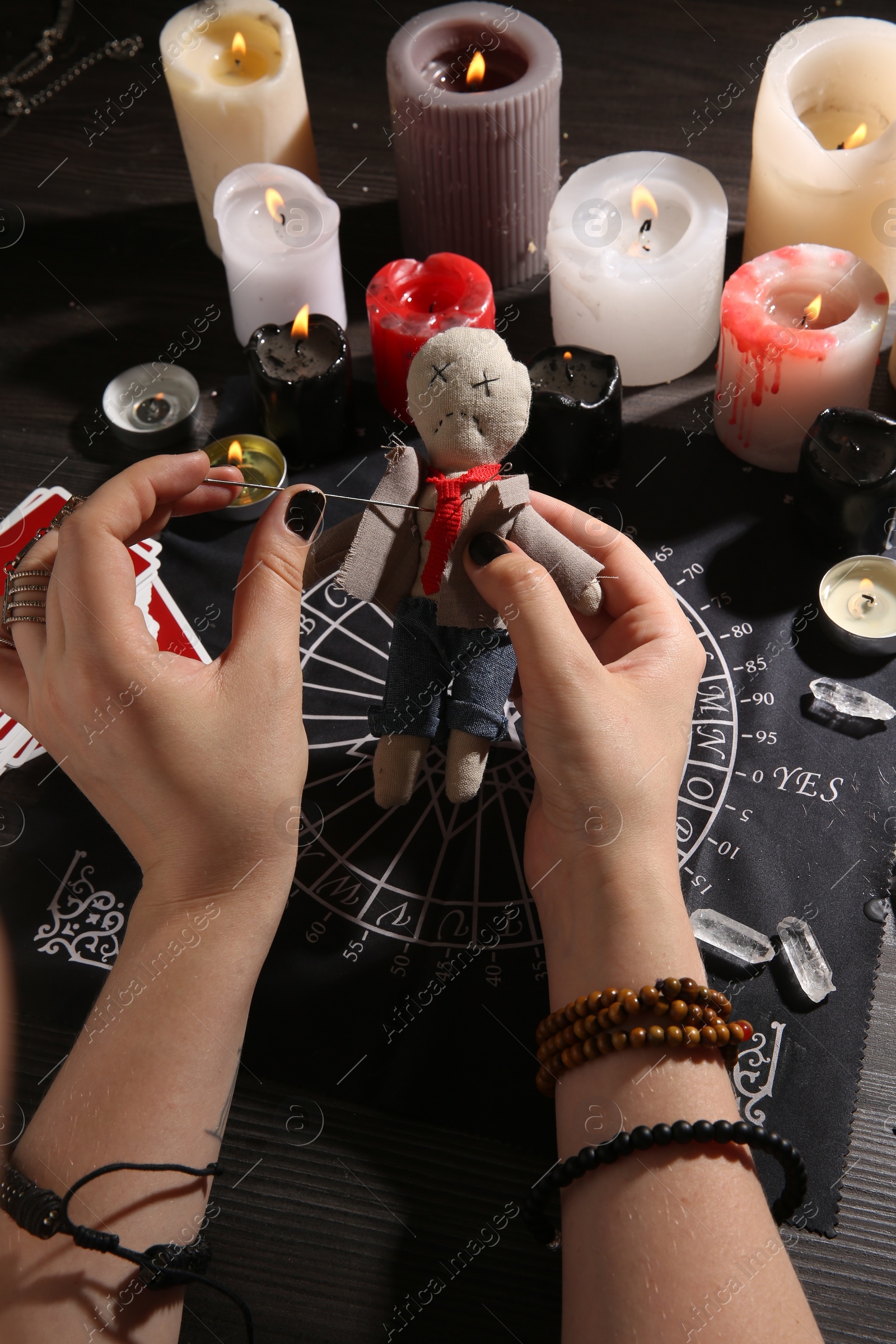 Photo of Woman stabbing voodoo doll with needle at table, closeup. Curse ceremony