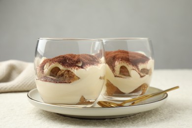 Delicious tiramisu in glasses and spoons on white table, closeup