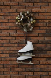 Pair of ice skates and beautiful Christmas wreath hanging on brick wall