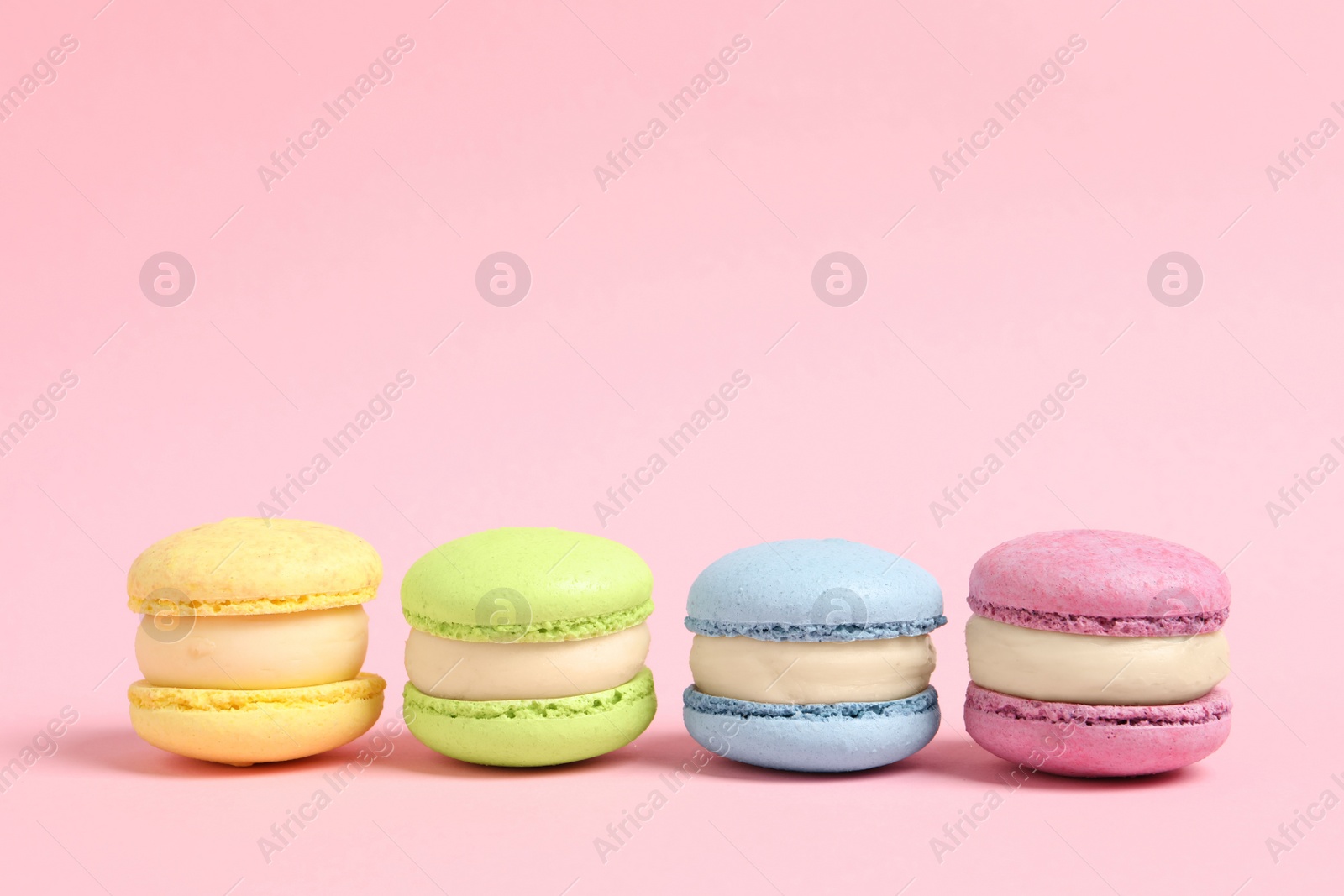 Photo of Delicious colorful macarons on pink background, space for text