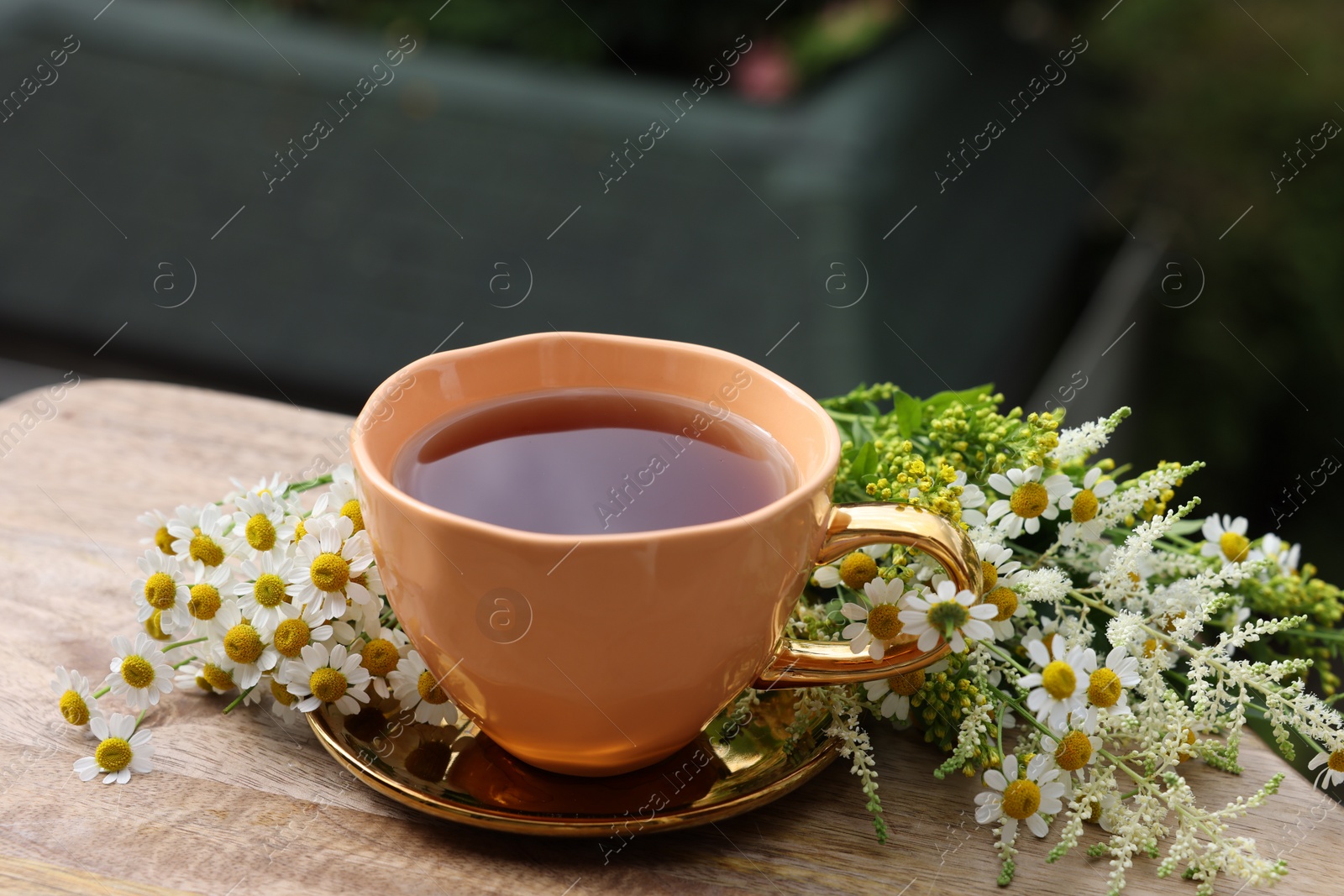 Photo of Cup of delicious chamomile tea and fresh flowers outdoors