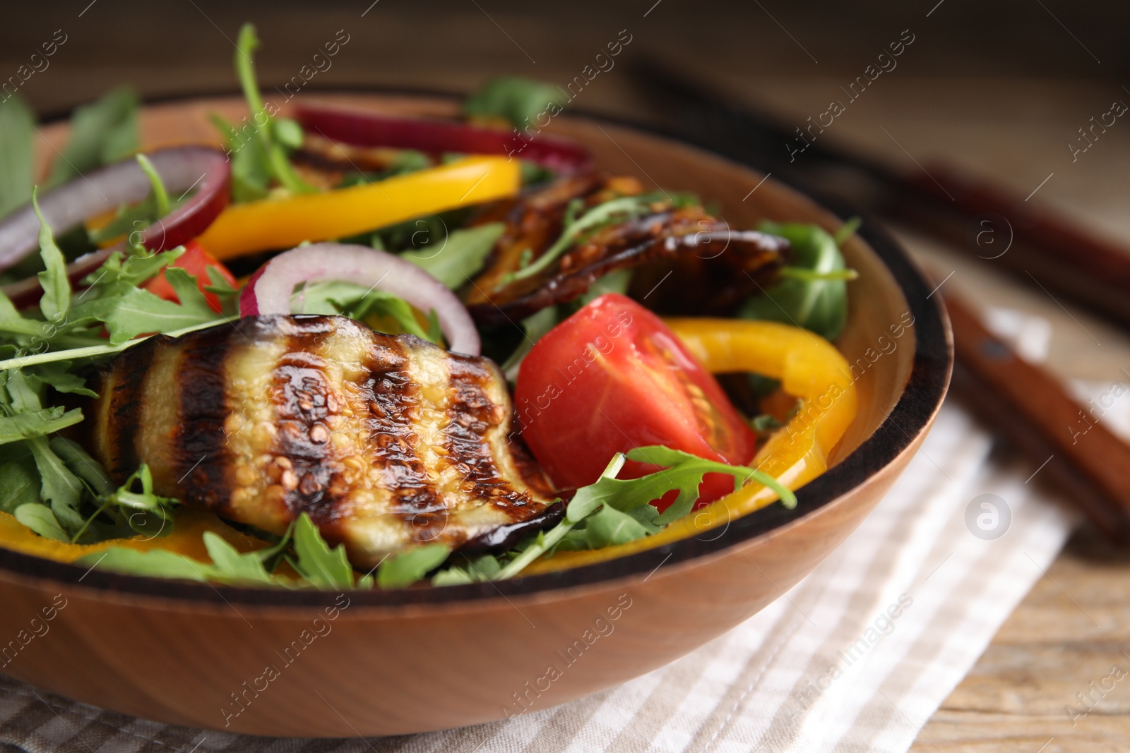 Photo of Delicious salad with roasted eggplant and arugula served on wooden table, closeup