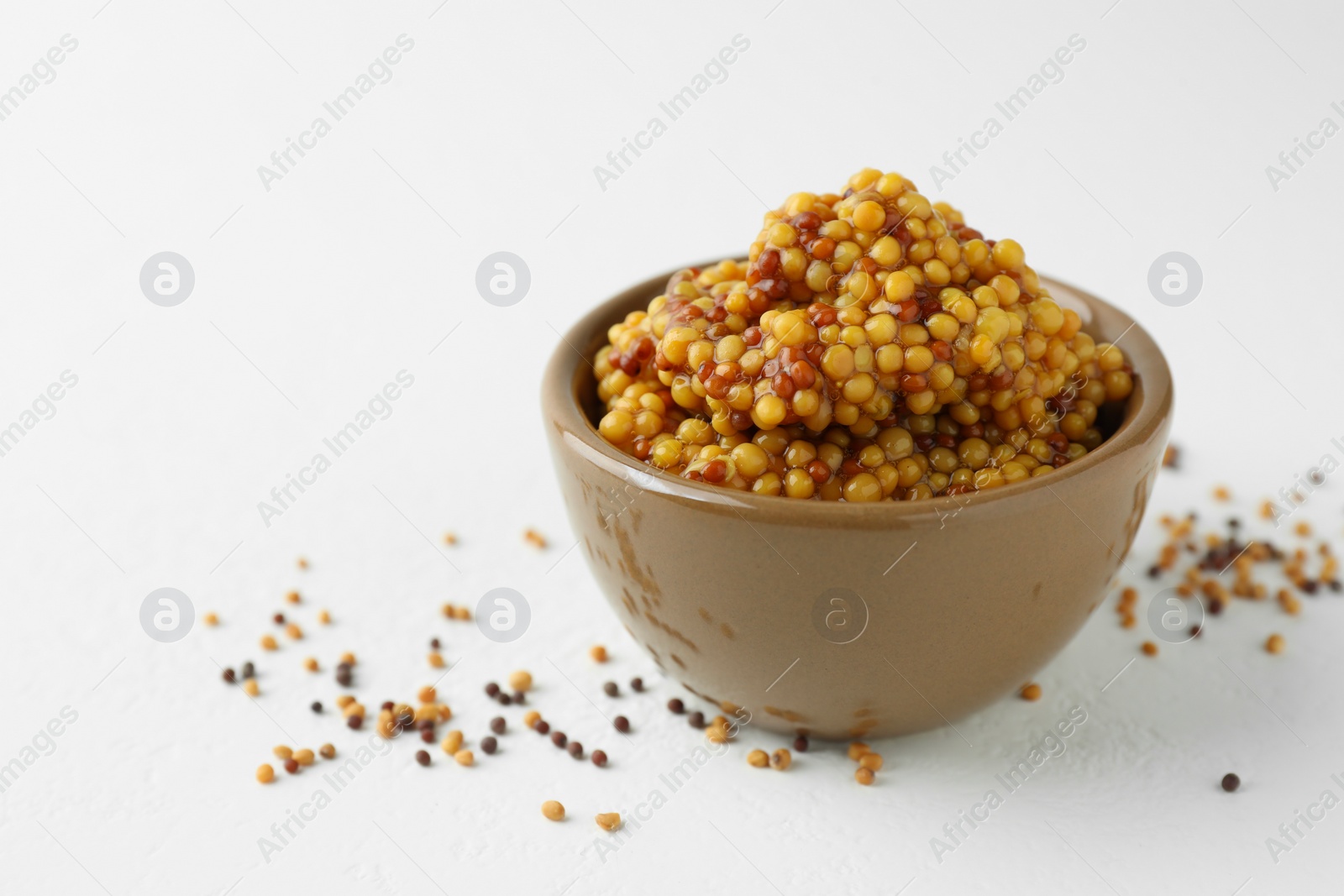 Photo of Fresh whole grain mustard in bowl and dry seeds on white table. Space for text