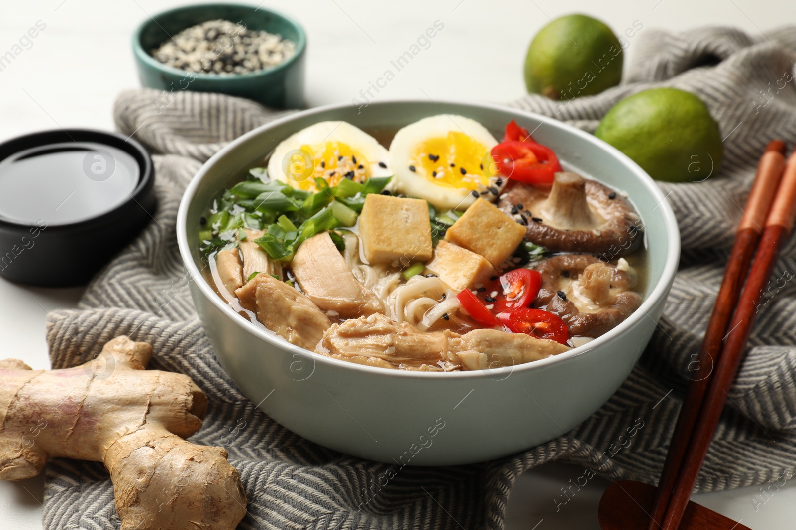 Photo of Bowl of delicious ramen, ingredients and chopsticks on white table, closeup. Noodle soup