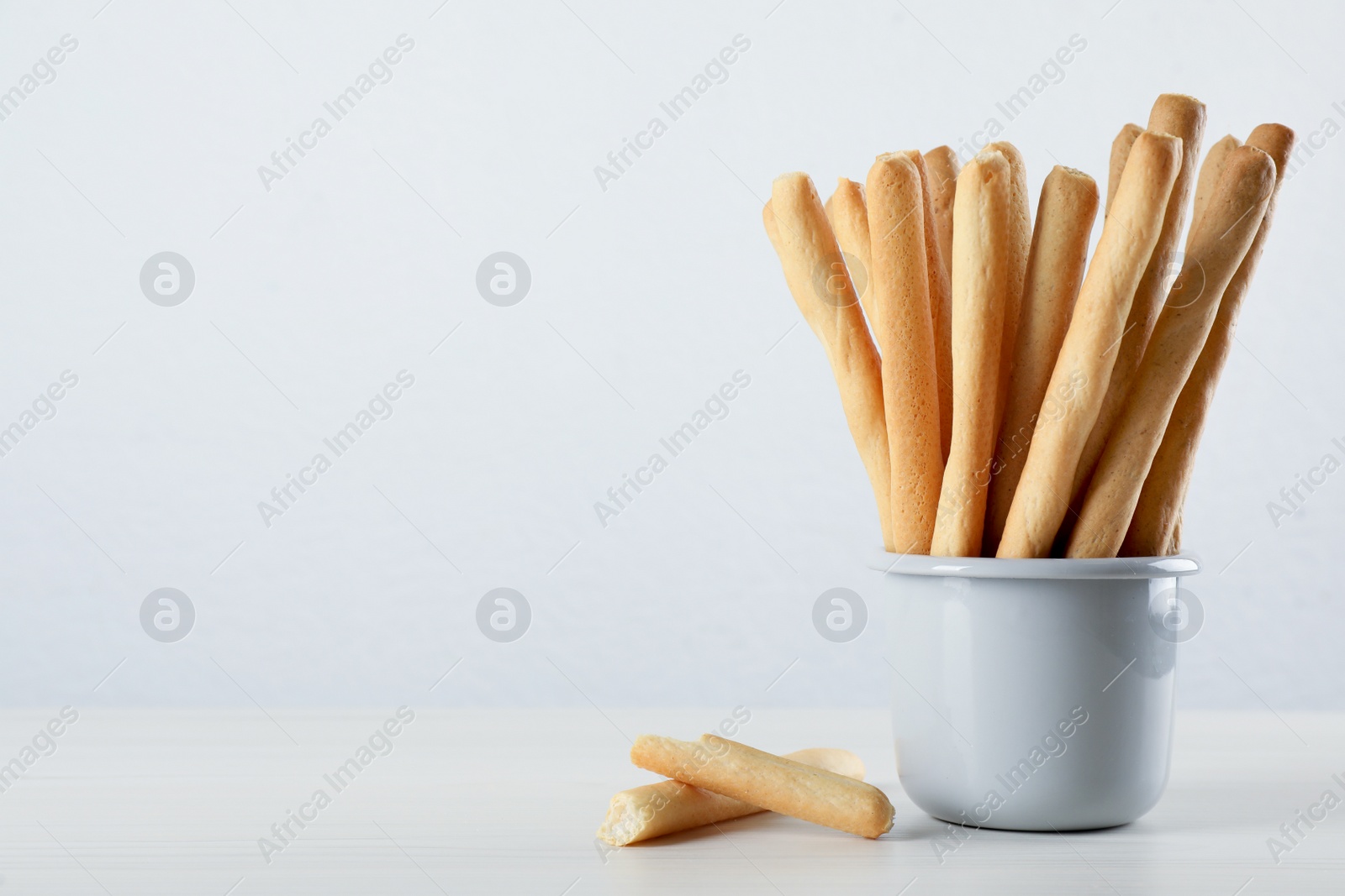 Photo of Delicious grissini sticks on white wooden table. Space for text