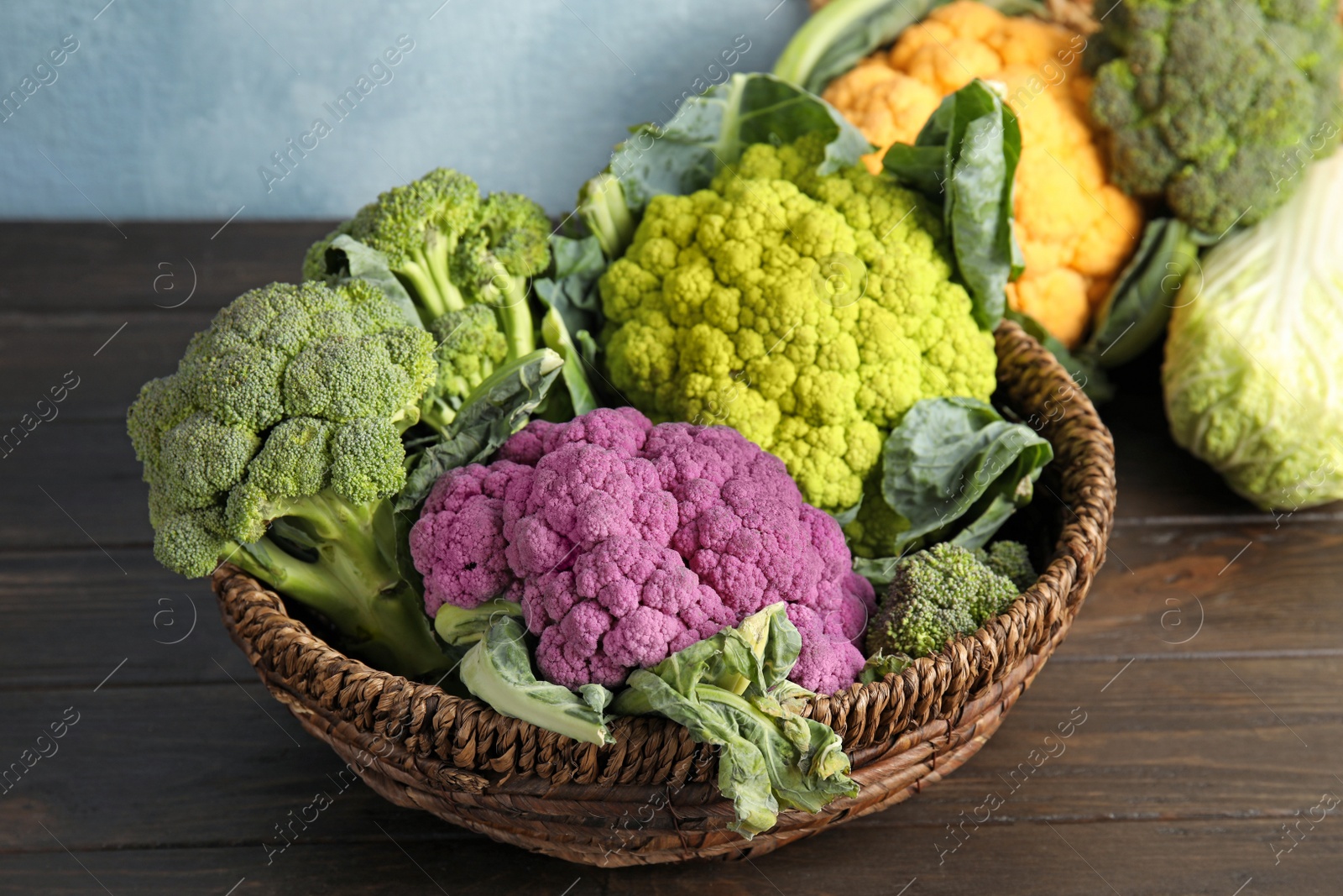 Photo of Wicker basket with different cabbages on wooden table. Healthy food