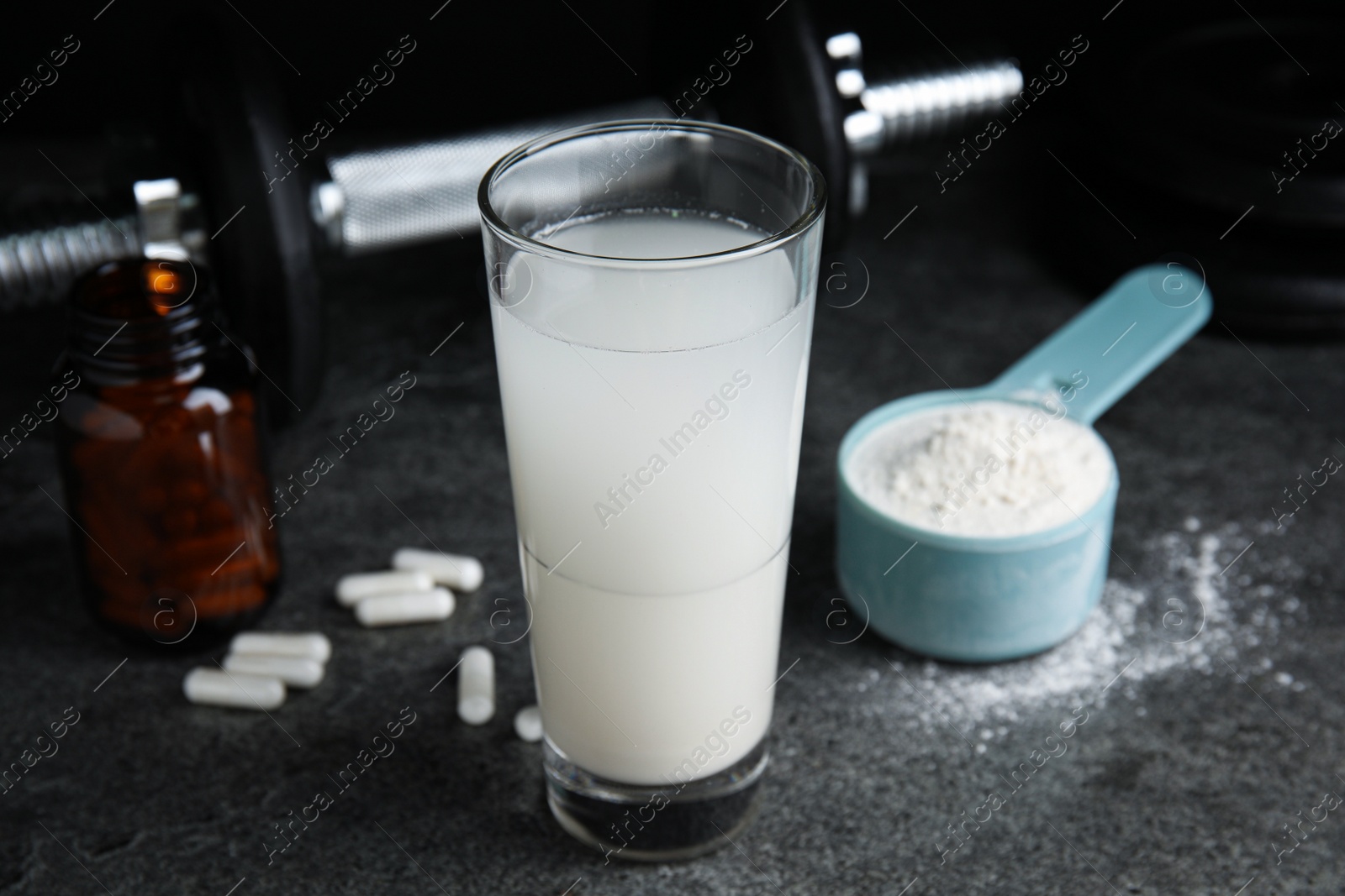 Photo of Amino acid shake, powder, pills and dumbbell on grey table