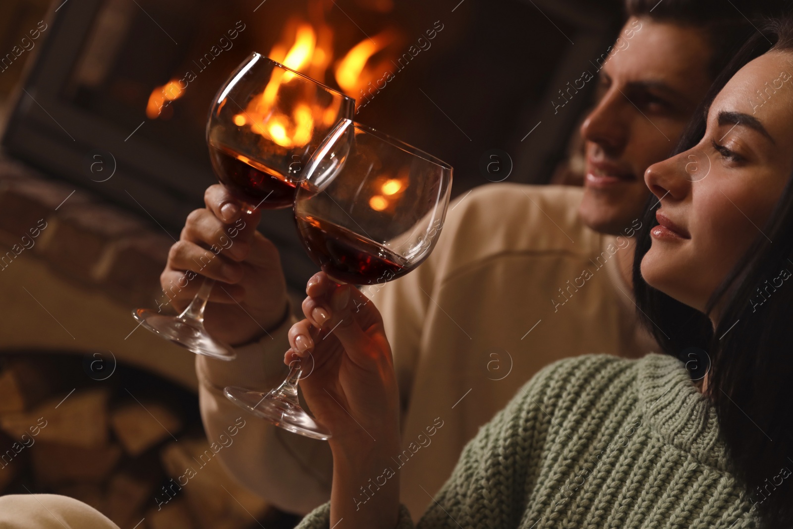 Photo of Lovely couple with glasses of wine near fireplace indoors, closeup. Winter vacation