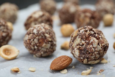 Photo of Delicious sweet chocolate candies and nuts on parchment paper, closeup