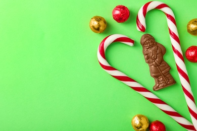 Flat lay composition with chocolate Santa Claus, candy canes and sweets on light green background, space for text