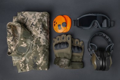 Tactical gloves, uniform and headphones on black background, flat lay. Military training equipment