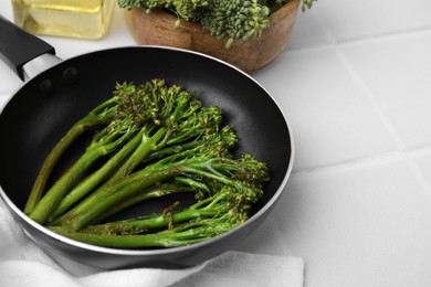 Photo of Frying pan with tasty cooked broccolini on white tiled table, closeup. Space for text