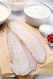 Different ingredients for batter and raw fish fillet on white table, above view