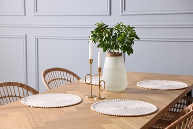 Photo of Vase with green branches and burning candles on wooden table in stylish dining room