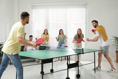 Happy friends playing ping pong together indoors