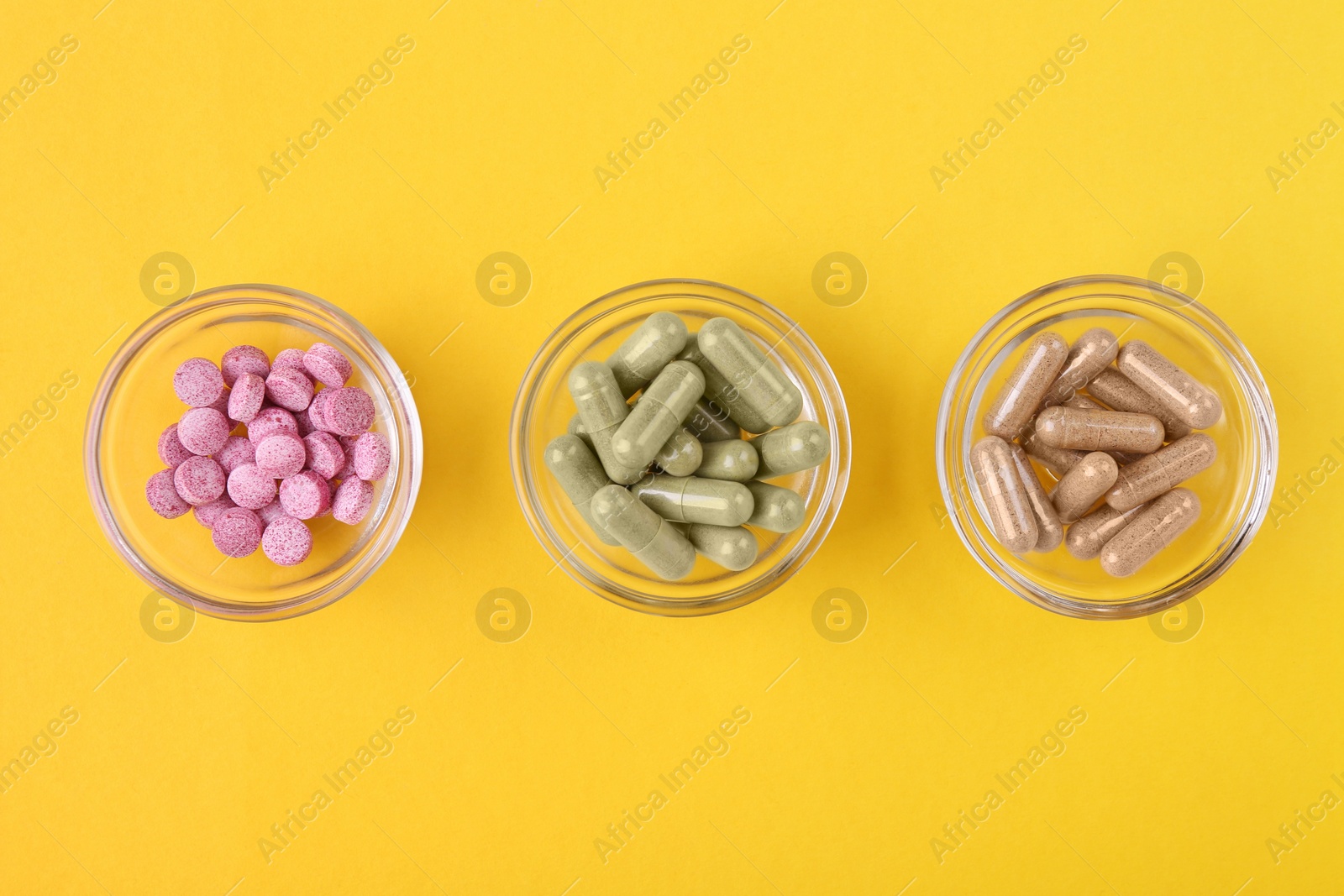 Photo of Different vitamin pills in glass bowls on yellow background, flat lay