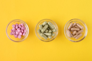 Photo of Different vitamin pills in glass bowls on yellow background, flat lay