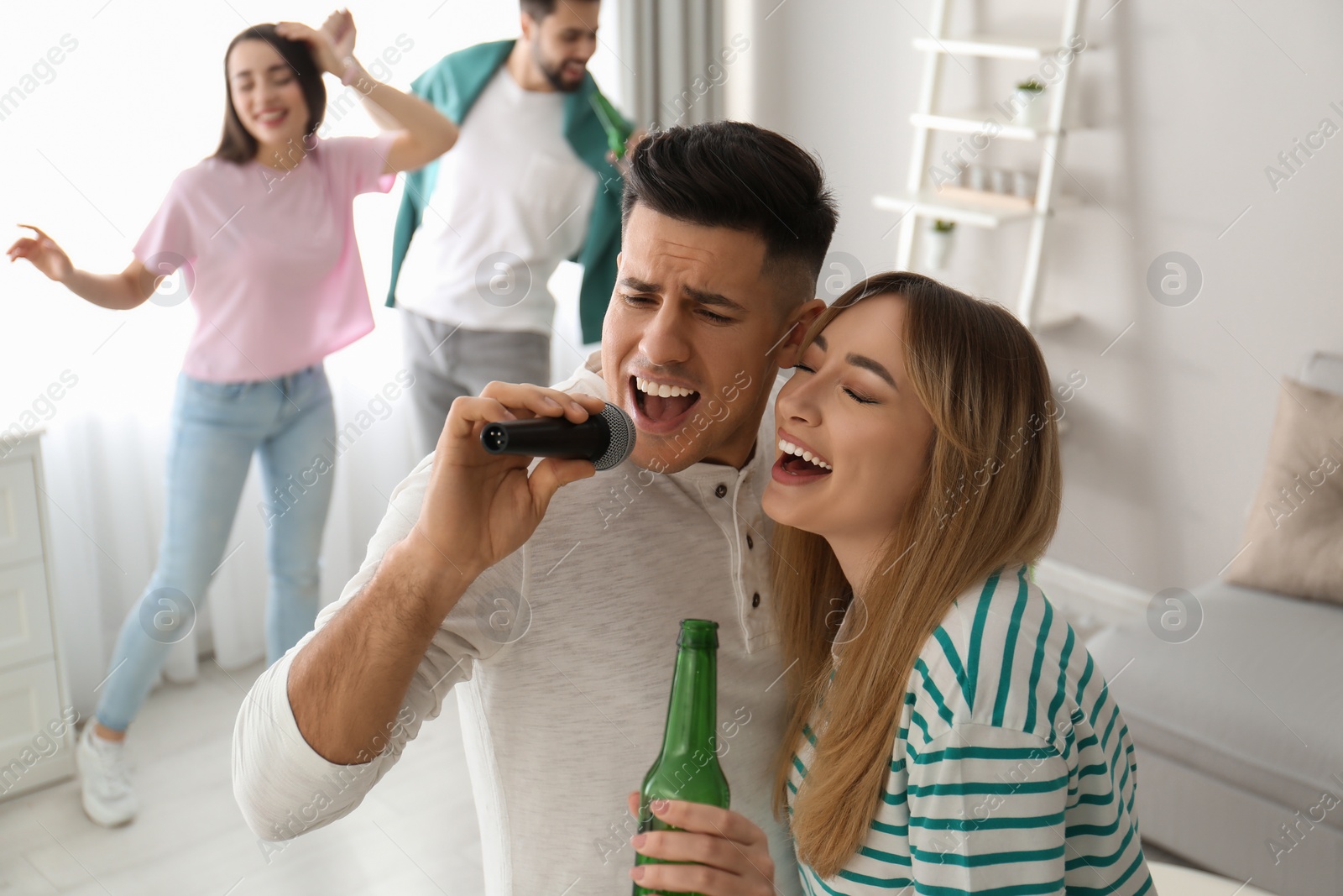 Photo of Happy couple singing karaoke with friends at home