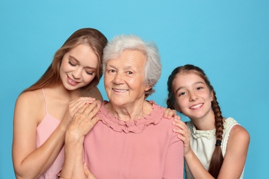 Happy sisters with their grandmother on light blue background