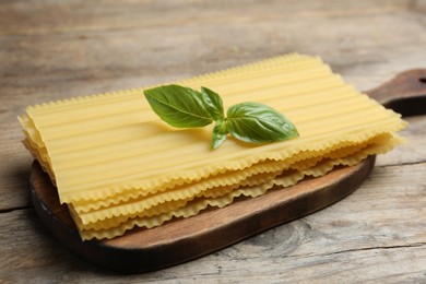 Uncooked lasagna sheets with basil on wooden table, closeup