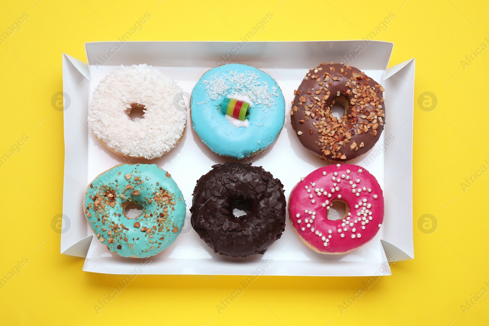 Photo of Box with tasty glazed donuts on yellow background, top view