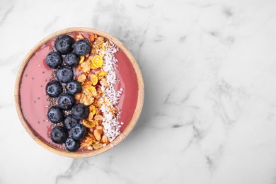 Photo of Bowl of delicious fruit smoothie with fresh blueberries, granola and coconut flakes on white marble table, top view. Space for text