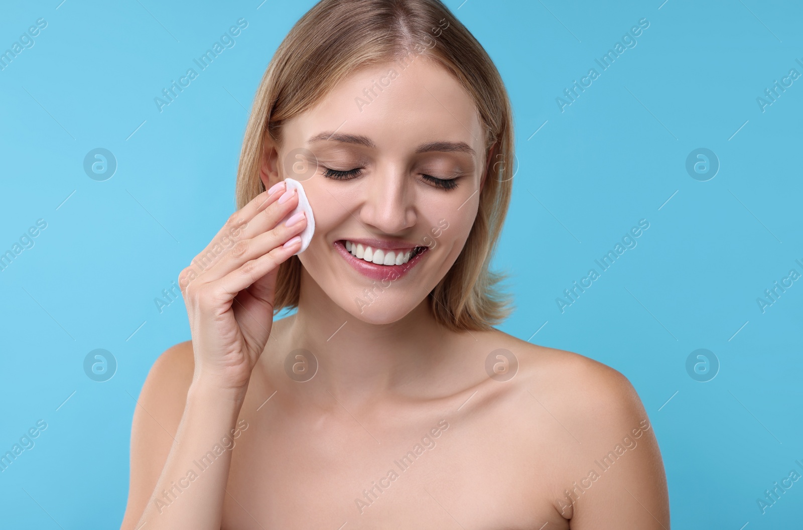 Photo of Young woman cleaning face with cotton pad on light blue background