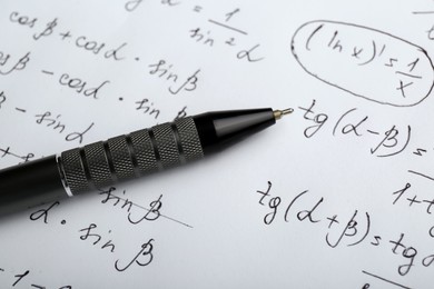 Sheet of paper with different mathematical formulas and pen, closeup