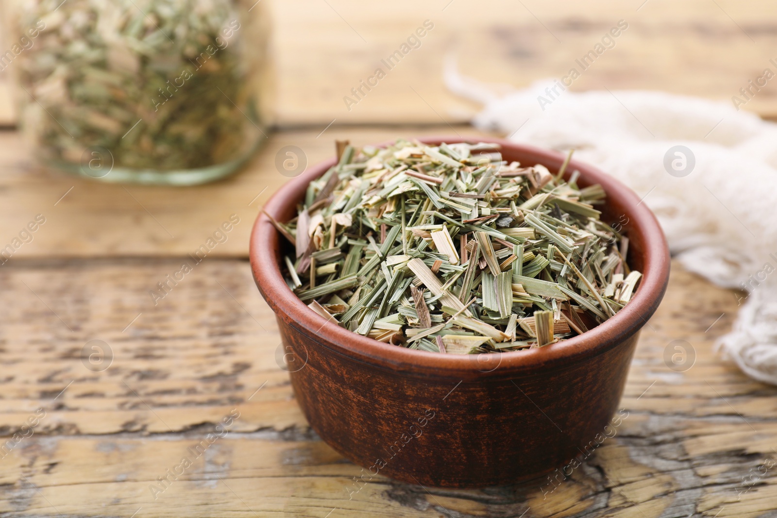 Photo of Bowl with aromatic dried lemongrass on wooden table, closeup