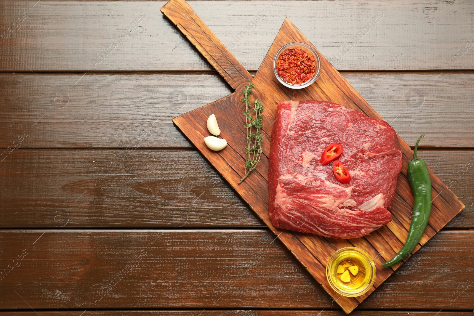 Photo of Fresh raw beef cut, spices and oil on wooden table, top view. Space for text