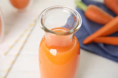 Photo of Freshly made carrot juice in glass bottle on white table, closeup