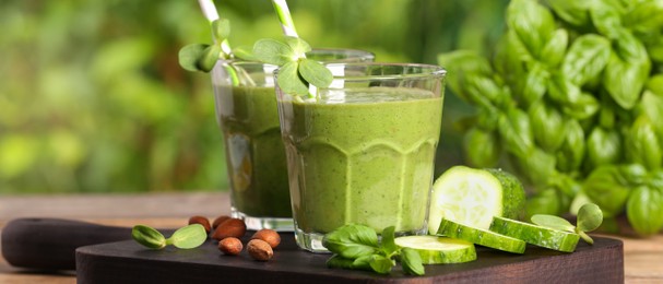 Glasses of fresh green smoothie and ingredients on wooden table outdoors. Banner design