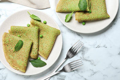 Tasty spinach crepes served on white marble table, flat lay