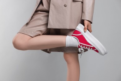 Woman posing in red classic old school sneakers on light gray background, closeup