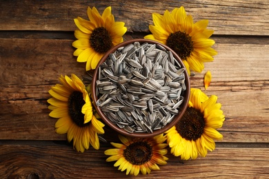 Photo of Raw sunflower seeds and flowers on wooden table, flat lay