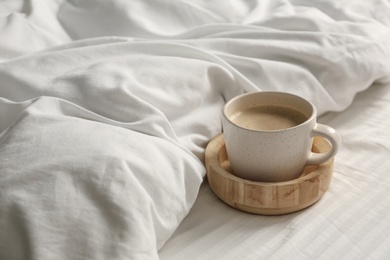 Photo of Cup of aromatic coffee on bed with soft blanket, closeup. Space for text