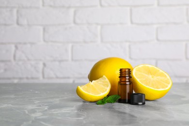 Photo of Bottle of essential oil with lemons and mint on grey marble table against white brick wall. Space for text