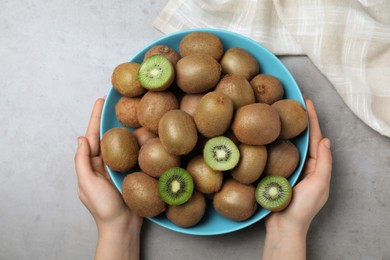 Photo of Woman holding bowl with fresh ripe kiwis at light grey table, top view