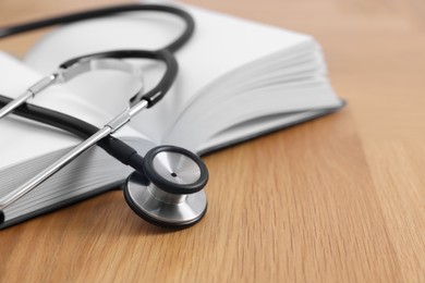Photo of Book and stethoscope on wooden table, closeup. Space for text