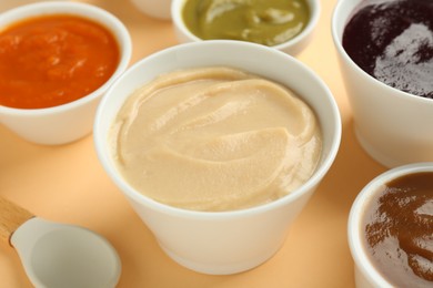 Photo of Bowls with healthy baby food and spoon on pale orange background, closeup