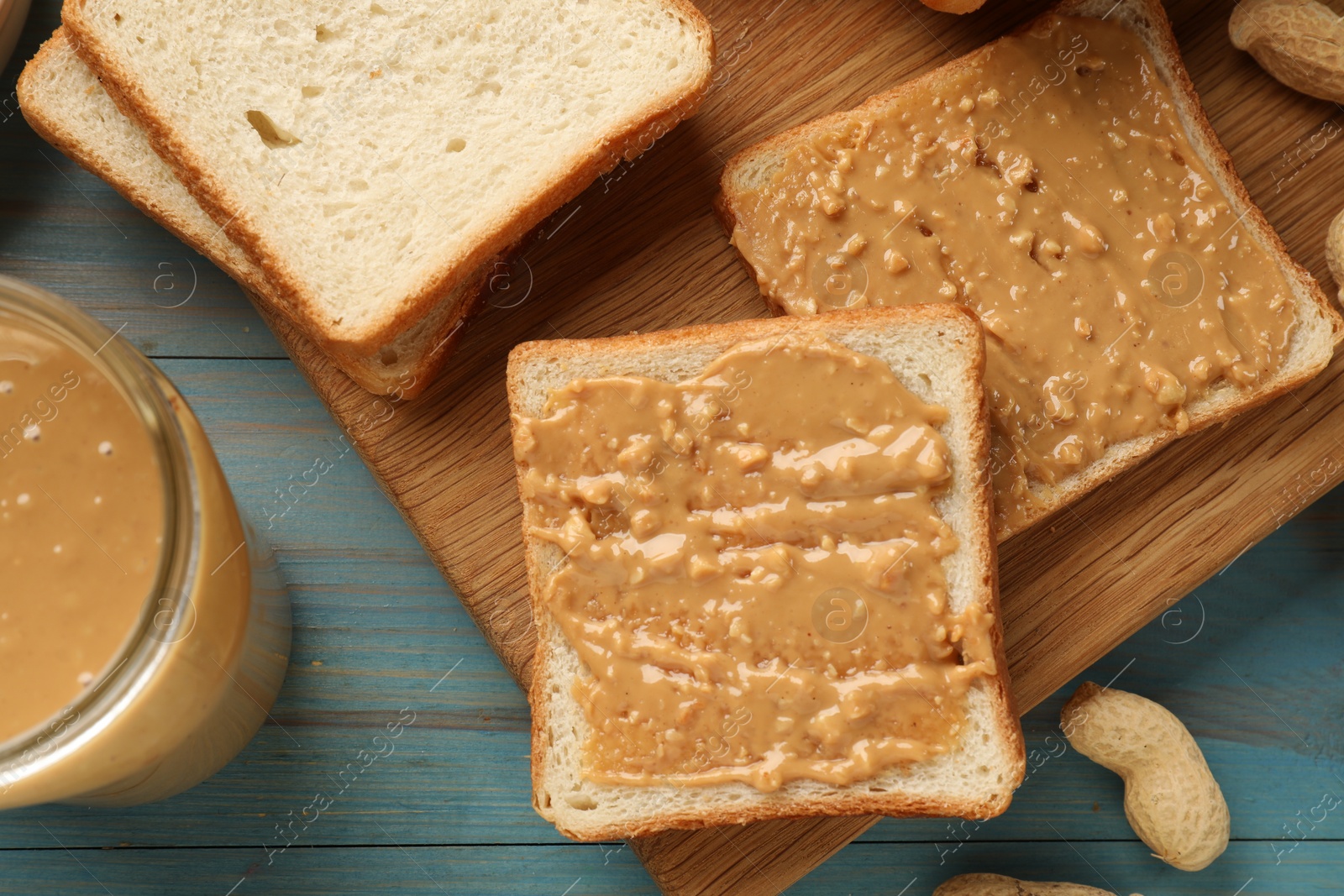 Photo of Delicious toasts with peanut butter on light blue wooden table, top view