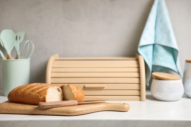 Photo of Wooden bread basket, freshly baked loaf on white marble table in kitchen