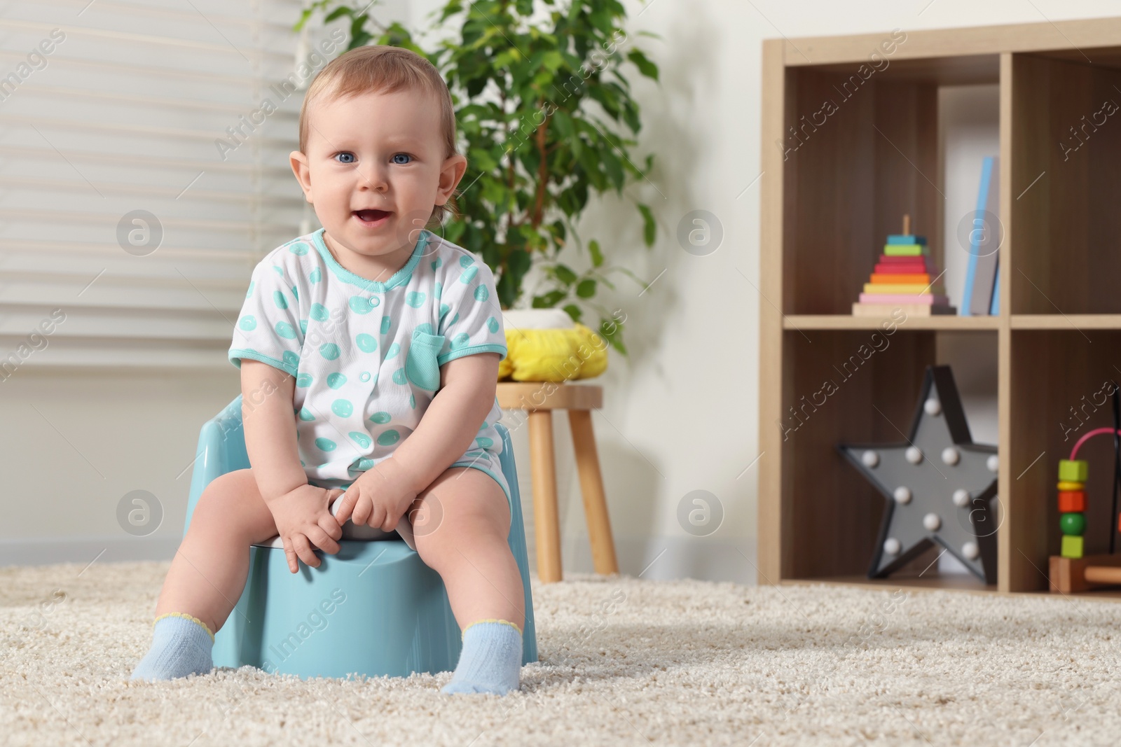 Photo of Little child sitting on plastic baby potty indoors. Space for text