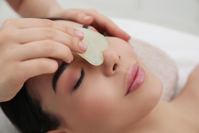 Photo of Young woman receiving facial massage with gua sha tool in beauty salon, closeup