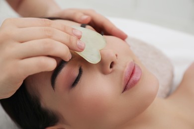 Young woman receiving facial massage with gua sha tool in beauty salon, closeup