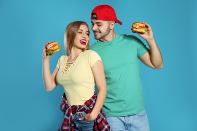 Photo of Happy couple with tasty burgers on color background