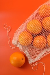 Net bag with fresh oranges on color background, top view