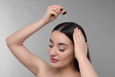 Photo of Young woman applying essential oil onto hair roots on light grey background