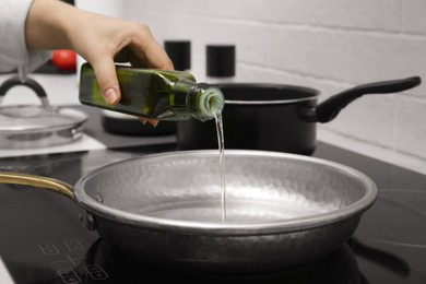 Photo of Woman pouring cooking oil from bottle into frying pan in kitchen, closeup